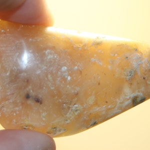 Peut inclure: Une pierre d'agate lisse de couleur brun clair avec des tourbillons et des inclusions blancs et gris. La pierre est translucide et a une finition polie.