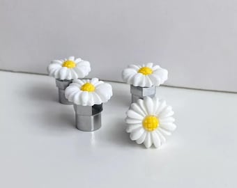 May include: Four white daisy flower-shaped car tire valve stem caps with yellow centers.