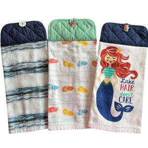 May include: Set of three kitchen towels with a nautical theme. One towel features a blue and white striped pattern, another has a green and white pattern with flip-flops, and the third has a mermaid with the text "Lake Hair don't care".