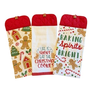 May include: Three hanging kitchen towels with red quilted tops and buttons. One features gingerbread men and trees, one has the text "LIFE IS SHORT EAT THE CHRISTMAS COOKIES", and one displays "BAKING SPIRITS BRIGHT" with gingerbread men and candy canes.
