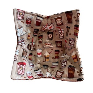 May include: A beige fabric pot holder with a coffee cup pattern. The pattern includes various coffee drinks, including lattes, espressos, and cappuccinos. The words "Espresso", "Latte", and "Coffee" are visible on the pot holder.