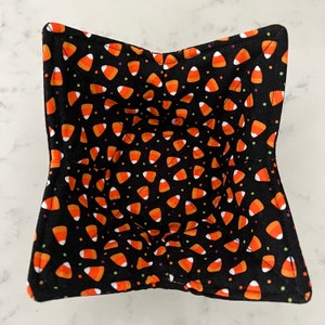 May include: A black fabric bowl with a candy corn pattern. The bowl is quilted and has a scalloped edge.
