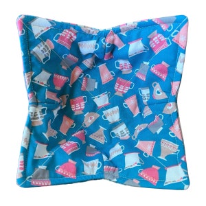 May include: A teal blue fabric pot holder with a quilted design. The fabric features a repeating pattern of pink, white, and brown teacups and teapots.
