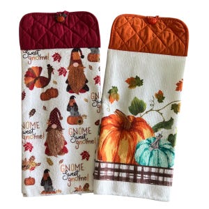 May include: Two kitchen towels with quilted tops. One towel features a turkey, gnomes, and the text "Sweet gnome!" The other towel has pumpkins and leaves. Both towels have a white background.