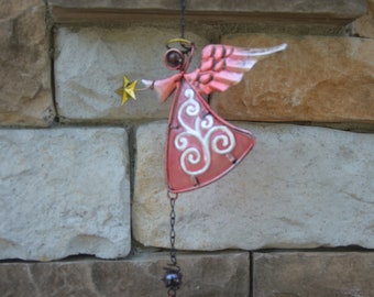 May include: A pink metal angel with white swirls and a gold star hanging from a chain with a brown bead at the bottom.