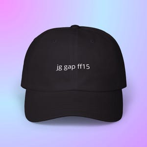 May include: Black baseball cap with a curved brim. The cap features the white text "jg gap ff15" centered on the front. The background is a gradient of pink and blue.