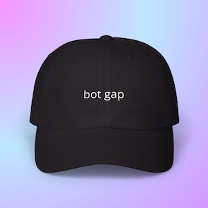 May include: Black baseball cap with a curved brim. The cap features the white text "bot gap" centered on the front. The background is a gradient of pink and blue.