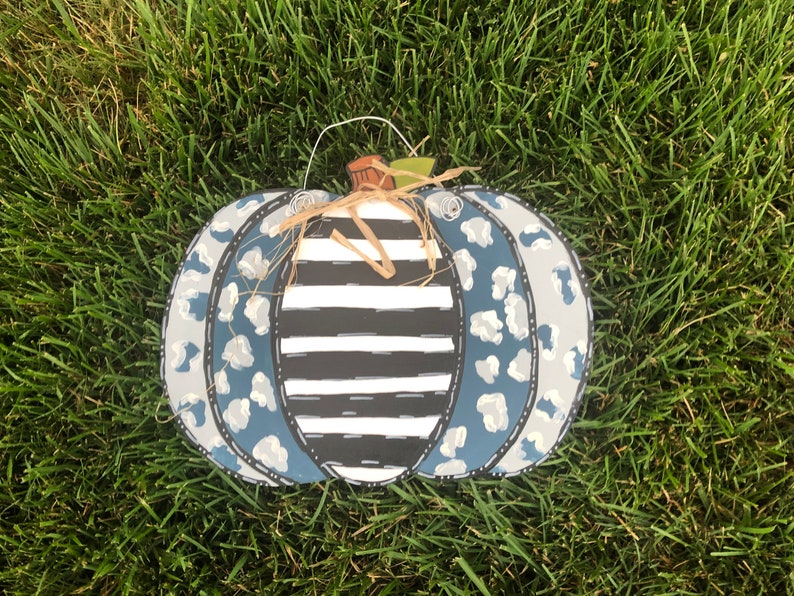 Puede incluir: Un colgador de puerta de calabaza azul y blanco con un centro a rayas blanco y negro. La calabaza est&aacute; decorada con un estampado de leopardo.