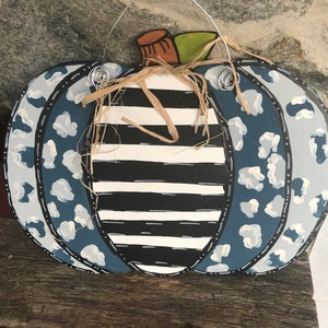 Puede incluir: Una calabaza rayada en blanco y negro con detalles de estampado de leopardo azul y blanco. La calabaza tiene un tallo marr&oacute;n y un lazo de paja.