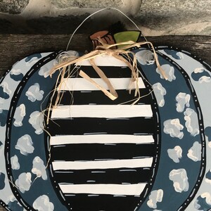 Puede incluir: Una calabaza a rayas azul y blanca con un dise&ntilde;o de estampado de leopardo azul y blanco. La calabaza tiene un lazo de paja y un colgador de alambre.