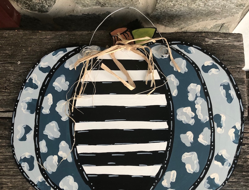 Puede incluir: Una calabaza a rayas azul y blanca con un dise&ntilde;o de estampado de leopardo azul y blanco. La calabaza tiene un lazo de paja y un colgador de alambre.