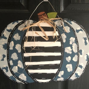 Puede incluir: Una calabaza a rayas azul y blanca con un dise&ntilde;o de estampado de leopardo azul y blanco. La calabaza est&aacute; decorada con un tallo marr&oacute;n y un lazo de paja.