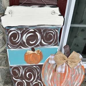 May include: A wooden coffee cup door hanger with a brown and white swirl design, a blue stripe, and a small orange pumpkin. A larger pumpkin with a burlap bow is attached to the side of the coffee cup.