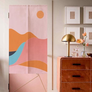 Pode incluir: Um par de divisórias de ambiente em tecido com um design abstrato de paisagem montanhosa impresso em rosa, laranja e azul. As divisórias estão penduradas em uma moldura de porta branca. Uma cômoda de couro marrom com três gavetas está em primeiro plano.