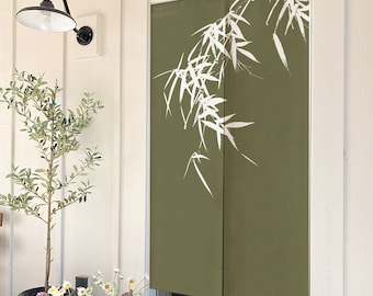 May include: A green door with a white bamboo design printed on it. The door is framed in white and is partially open. A small olive tree is in a pot in front of the door.