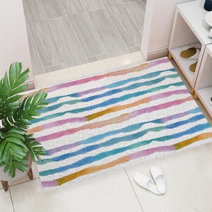 May include: A colorful striped rug with a white background and blue, yellow, pink, and orange stripes. The rug is made of a soft, textured material and has a subtle watercolor effect.