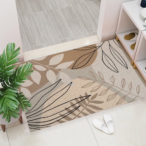 May include: A beige and brown doormat with a black and white abstract leaf design. The doormat is made of a soft, textured material.