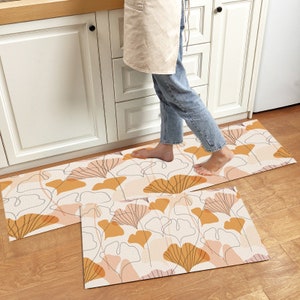 May include: Two kitchen runner rugs with a floral pattern in shades of brown, orange, and white. The rugs are placed on a wooden floor.