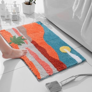 May include: A colorful bath mat with a desert landscape design featuring a palm tree, mountains, and a sun. The mat is made of soft, absorbent material and is perfect for adding a touch of style to your bathroom.