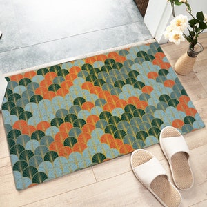 Puede incluir: Una alfombra de entrada azul, verde y naranja con un diseño geométrico. La alfombra de entrada está hecha de un material suave y texturizado y tiene un brillo sutil.