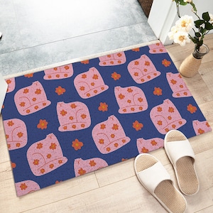 May include: A blue and pink doormat with a repeating pattern of pink cats with red flowers. The cats are wearing hats and have a floral pattern on their bodies.