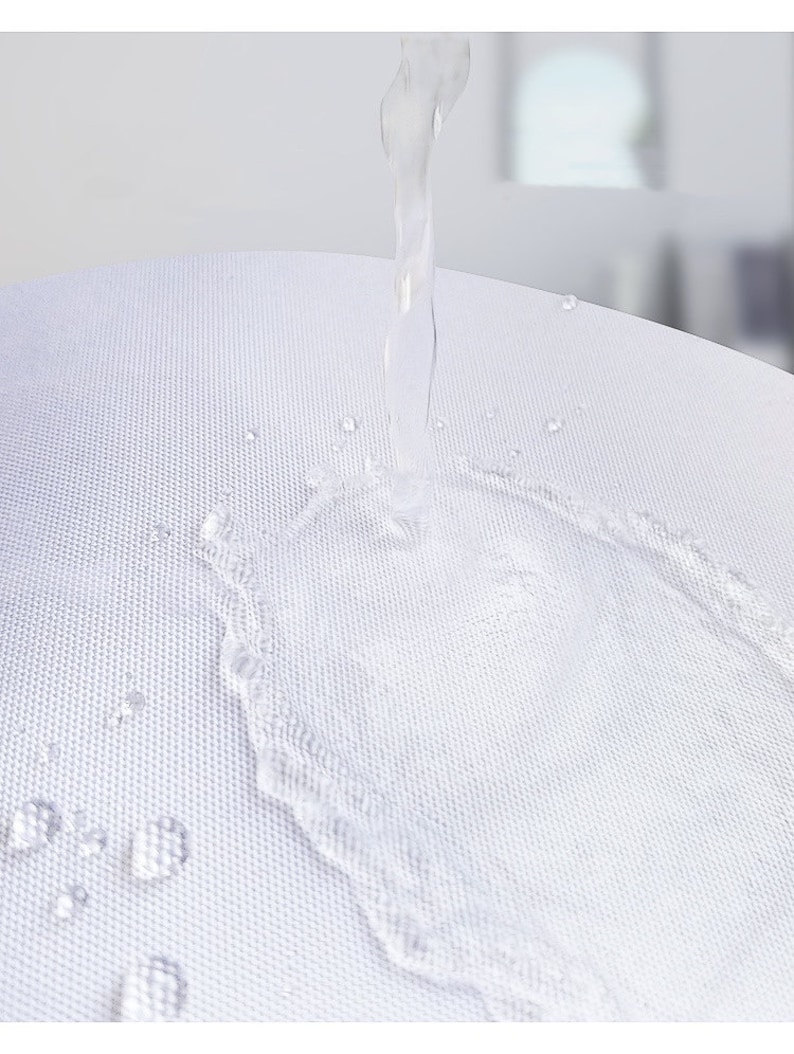 K&ouml;nnte beinhalten: Nahaufnahme eines wei&szlig;en Stoffes mit Wassertropfen und einem Wasserstrahl, der herunterflie&szlig;t. Der Stoff hat eine strukturierte Oberfl&auml;che, und das Wasser erzeugt einen dynamischen visuellen Effekt. Das Bild hebt die F&auml;higkeit des Stoffes hervor, Wasser abzuweisen.