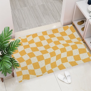May include: A yellow and white checkered doormat with a wavy pattern. The doormat is made of a textured material and is placed in front of a white door.
