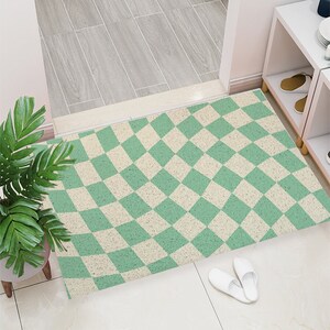 May include: A green and white checkered doormat with a wavy pattern. The doormat is made of a textured material and has a subtle speckled appearance.