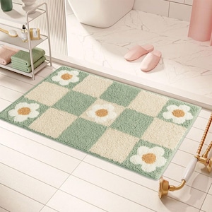 May include: A rectangular bath mat with a checkerboard pattern of light green and cream squares. White daisy flower designs with yellow centers are placed on the mat. The mat is on a tiled floor.