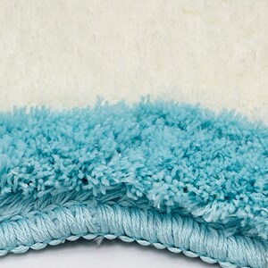 May include: Close-up of a light blue bath mat with a white fluffy top and a blue fringe border.