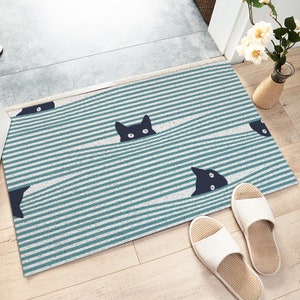 May include: A blue and white striped doormat with black cat silhouettes peeking out from behind the stripes. The cat silhouettes have white eyes.