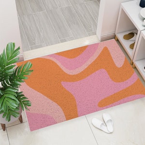 Könnte beinhalten: Eine abstrakte Türmatte mit welligem Muster in Rosa und Orange.