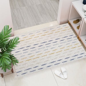 May include: A white doormat with a geometric pattern of blue and yellow lines. The doormat is placed on a tiled floor in a hallway.