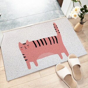 May include: A white doormat with a pink and black cat illustration. The cat has closed eyes and a striped tail. The doormat has a speckled texture.