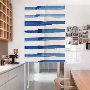 Può includere: Una tenda a strisce bianche e blu con un design simile all'acquerello. La tenda è appesa in una cucina con un tavolo e sedie in legno.