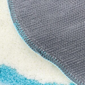 May include: Close-up of the underside of a blue and white bath mat. The mat has a non-slip backing with a grid pattern.