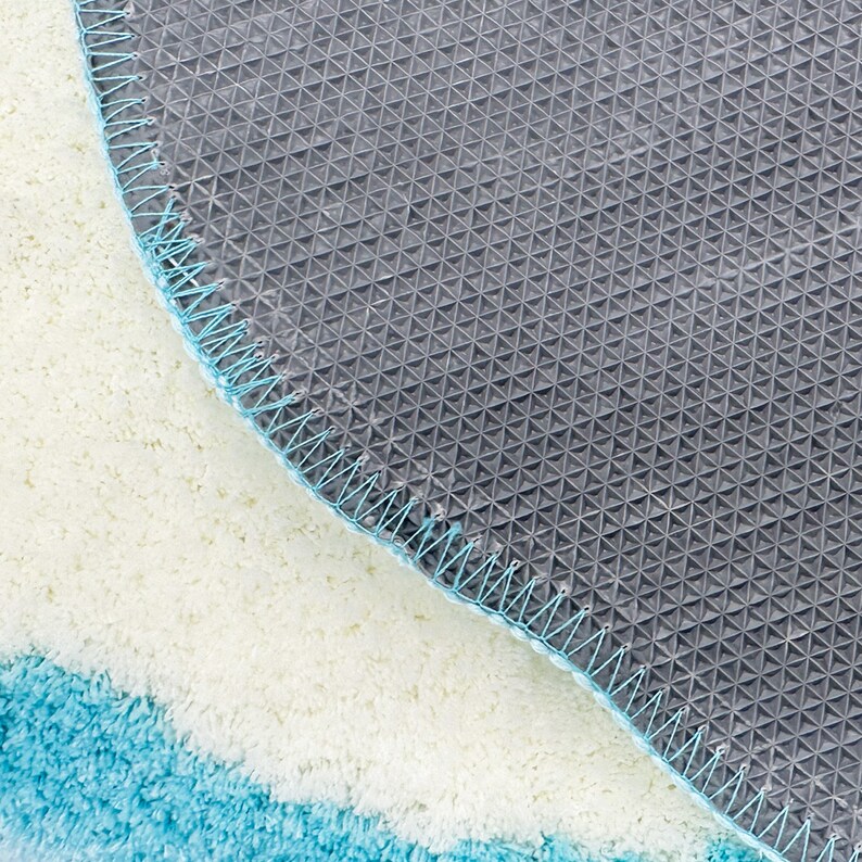 May include: Close-up of the underside of a blue and white bath mat. The mat has a non-slip backing with a grid pattern.