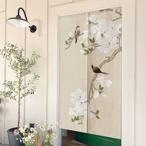 May include: A white door with a beige fabric room divider featuring a floral design with white magnolia blossoms and two brown birds. The divider is hung on a white door frame.