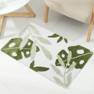 May include: A white bath mat with a green leaf design. The leaves are in a variety of shades of green and have a fluffy texture.