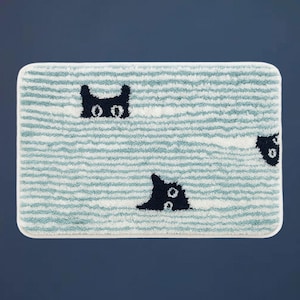 May include: Rectangular bath mat with a light blue and white striped design. The mat features black cat faces peeking out from the stripes. It has a white border and is designed for bathroom use.