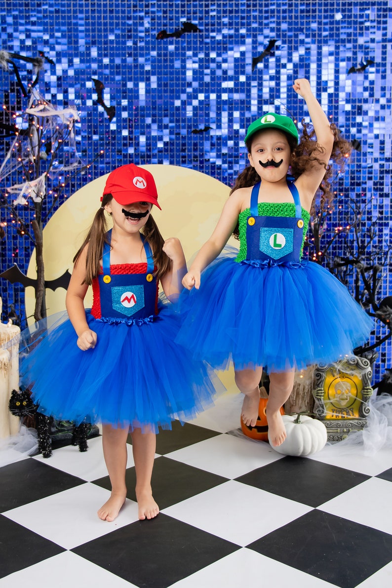 Puede incluir: Dos ni&ntilde;os disfrazados de Mario y Luigi para Halloween. Llevan tut&uacute;s de tul azul con monos rojos y verdes. La ni&ntilde;a disfrazada de Mario lleva un sombrero rojo con una 'M' y un bigote negro. La ni&ntilde;a disfrazada de Luigi lleva un sombrero verde con una 'L'. Est&aacute;n de pie sobre un suelo de ajedrez negro y blanco.