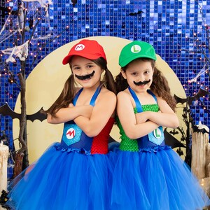 Puede incluir: Dos ni&ntilde;os disfrazados de Mario y Luigi para Halloween. Llevan tut&uacute;s azules y tienen bigotes falsos. El fondo es una pared azul brillante con una luna y murci&eacute;lagos.