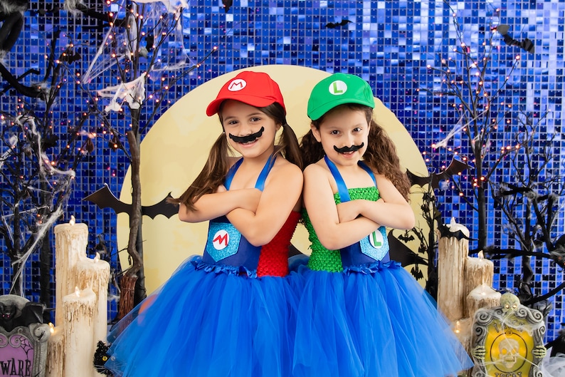 Puede incluir: Dos ni&ntilde;os disfrazados de Mario y Luigi para Halloween. Llevan tut&uacute;s azules y tienen bigotes falsos. El fondo es una pared azul brillante con una luna y murci&eacute;lagos.