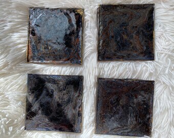 May include: Set of four square coasters with a black and gold marbled design. The coasters have a glossy finish and are ideal for protecting surfaces from heat and spills.