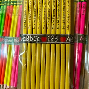 May include: A close-up of a package of yellow pencils with green and pink eraser tops. The pencils are labeled "Mrs. Mulligan 6th Grade". There are also some pink and yellow pencils in the background.