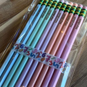 May include: A pack of ten personalized pencils with the name "MaryBeth" printed on each pencil. The pencils are in a variety of pastel colors, including light blue, light green, lavender, and pink. The pencils have green and yellow stripes near the eraser.
