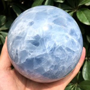 Könnte beinhalten: Eine große, hellblaue Cölestin-Kugel mit einer glatten, polierten Oberfläche. Die Kugel hat ein wolkiges, durchscheinendes Aussehen mit einem weißen Inneren.