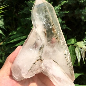 Peut inclure: Un grand amas de cristal de quartz clair avec une apparence naturelle et brute. Le cristal a une forme pointue et est recouvert de petites inclusions sombres.