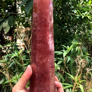 May include: A large, deep red crystal point with a faceted, pointed top. The crystal is translucent and has a slight shimmer.