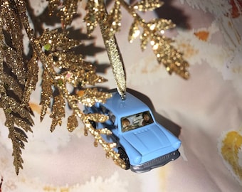 Könnte beinhalten: Ein blauer Ford Anglia Auto-Anhänger mit weißem Dach und silbernen Zierleisten. Das Auto hat einen Weihnachtsbaumschmuck-Haken oben. Das Auto ist mit einer Szene von Harry Potter und Ron Weasley im Auto verziert.